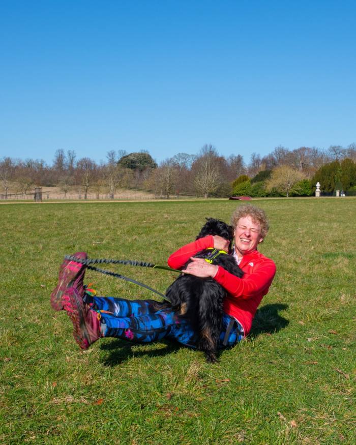 A female canicrosser hugging her dog on a field 