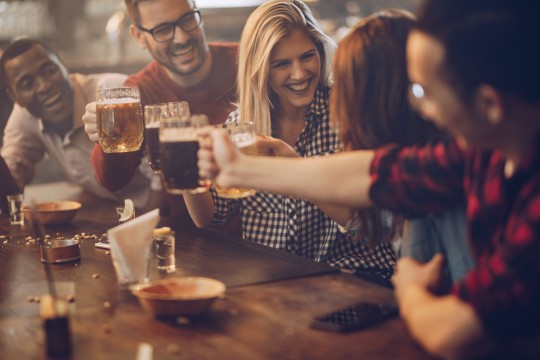 Can you go to the pub while you?re off sick from work? Cheerful friends toasting with beer and having fun in a bar. Focus is on blond woman talking to her friend.