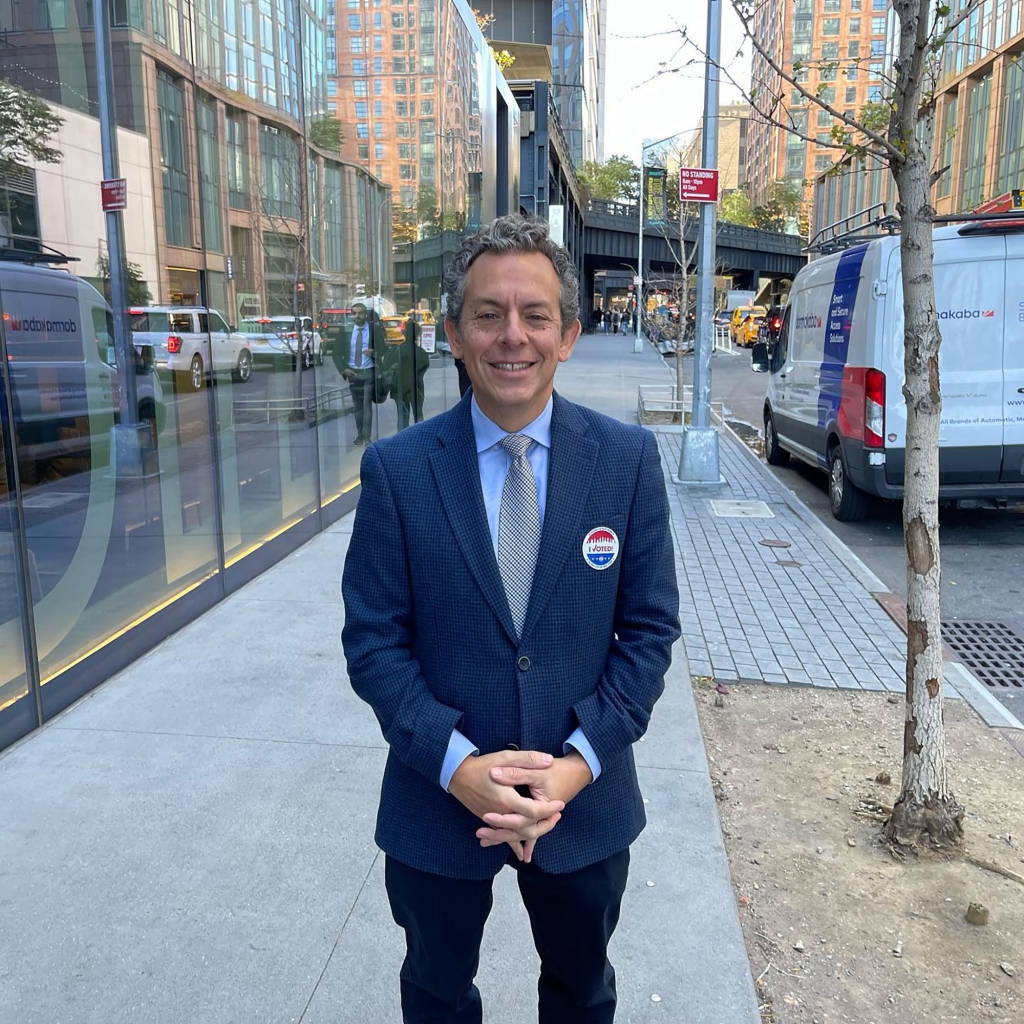 Simone in a blue suit standing on a sidewalk next to a small tree