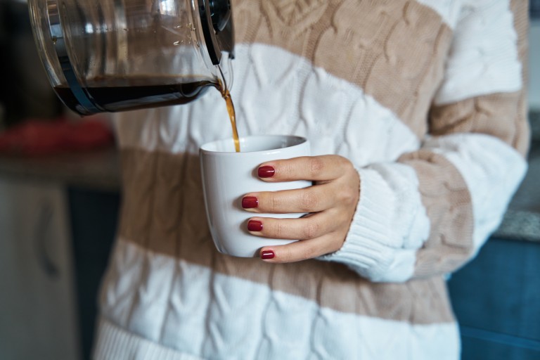 Woman pouring herself a mug of hot filtered coffee from a glass pot at home