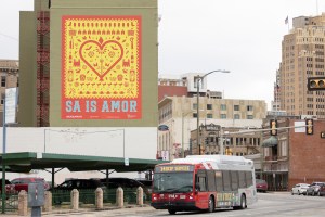 A VIA bus travels north on Broadway past the SA is Amor mural created by the Art Everywhere campaign of Centro.