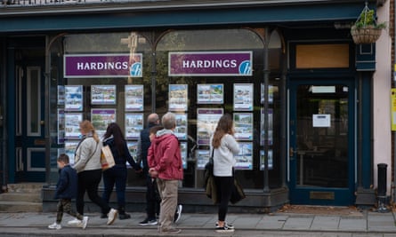 People walking past and looking in an estate agent;’s window, seen from the other side of the street