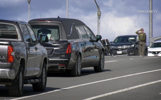 A deputy salutes as a procession of law enforcement escorts...