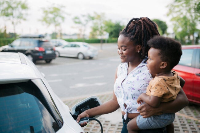 iStock-1412460130 problems with electric cars Mother holding her son while charging her electric vehicle