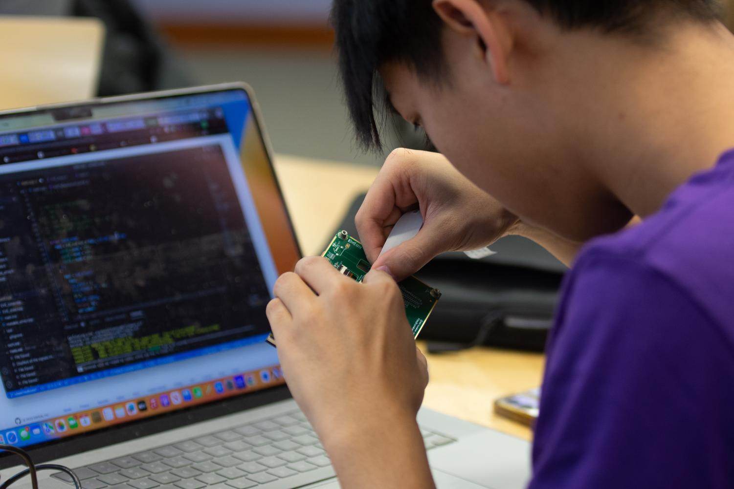 A+student+in+a+purple+t-shirt+works+on+a+green+circuit+board.