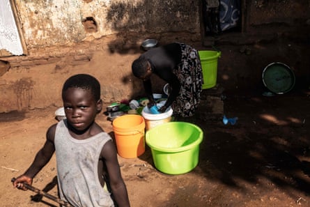 Woman washing utensils outside her home, with child in foreground.