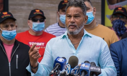 man speaks at mic in front of group of men wearing masks