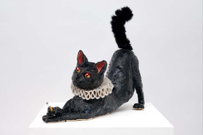 A black ceramic cat stretching its front legs out, with a cigarette in one paw