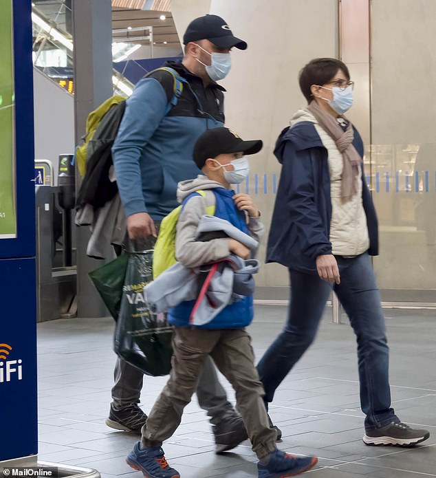 A family of three are pictured wearing face masks while walking around London Bridge today, April 28, 2023