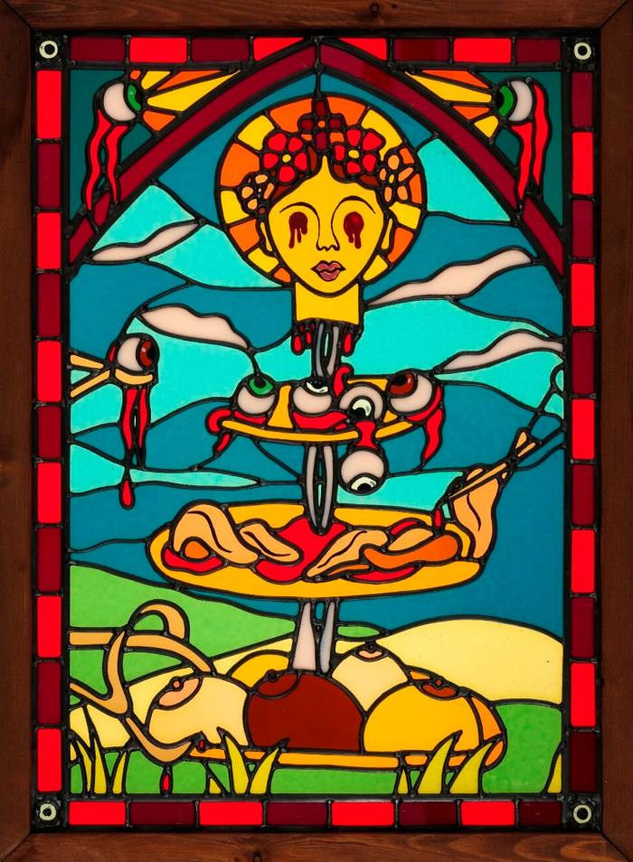 Stained glass in an ecclesiastical style with a cake stand laden with amputated breasts and plucked-out eyes with a head on the top