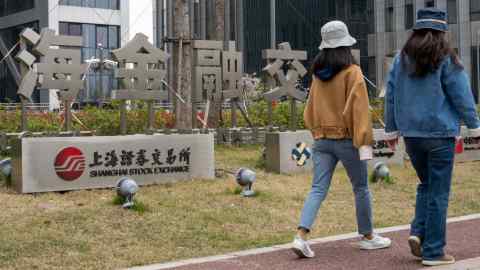 Women walk past a signage for the Shanghai Stock Exchange