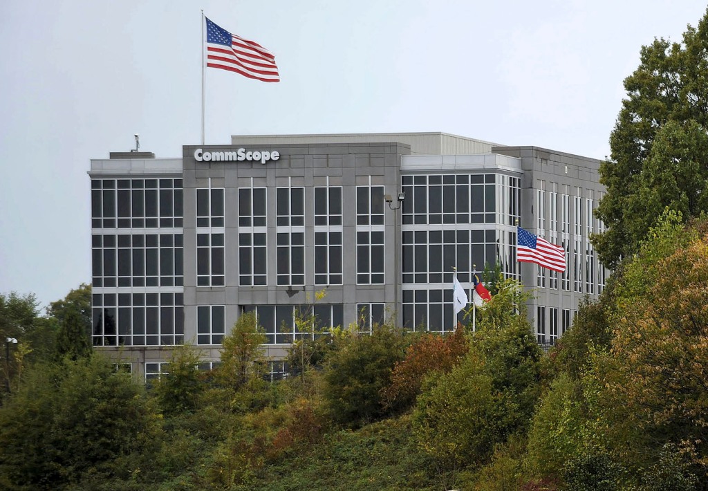 a photo of CommScope's headquarters in the distance with a U.S. flag over its headquarters surrounded by trees and other greenery