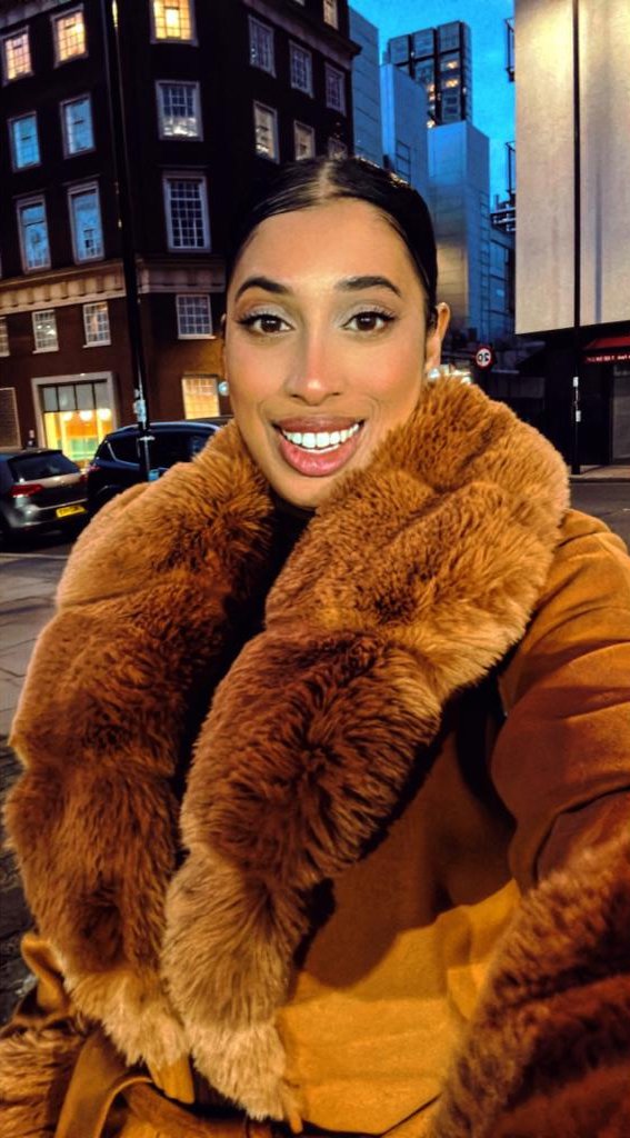 Lilufa Uddin, a young woman wearing a large fur-style coat, poses in a selfie