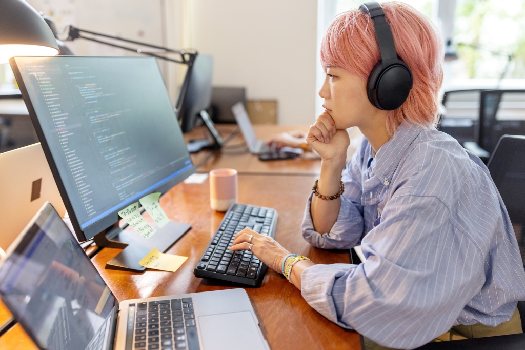 Woman coding working with multiple screens examining the code.