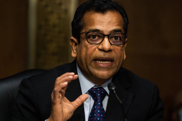 Sudhakar Ramakrishna wearing glasses and suit and tie gestures with his left hand while talking