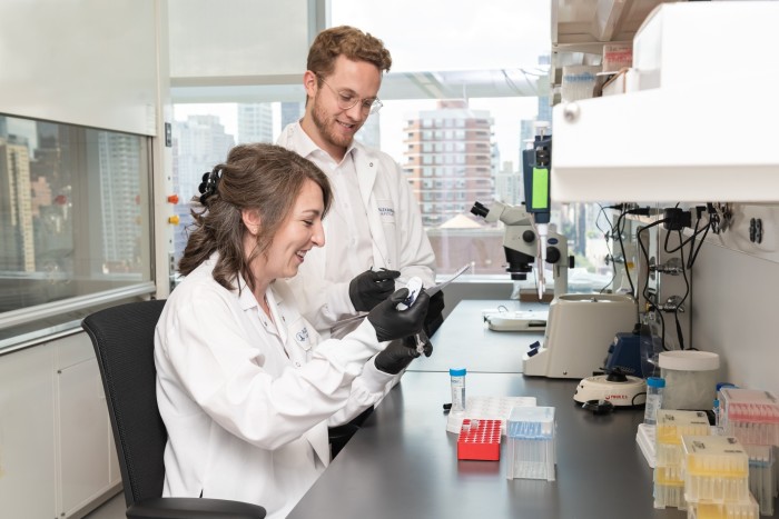 Two scientists in white coats lexamine test tubes in a lab