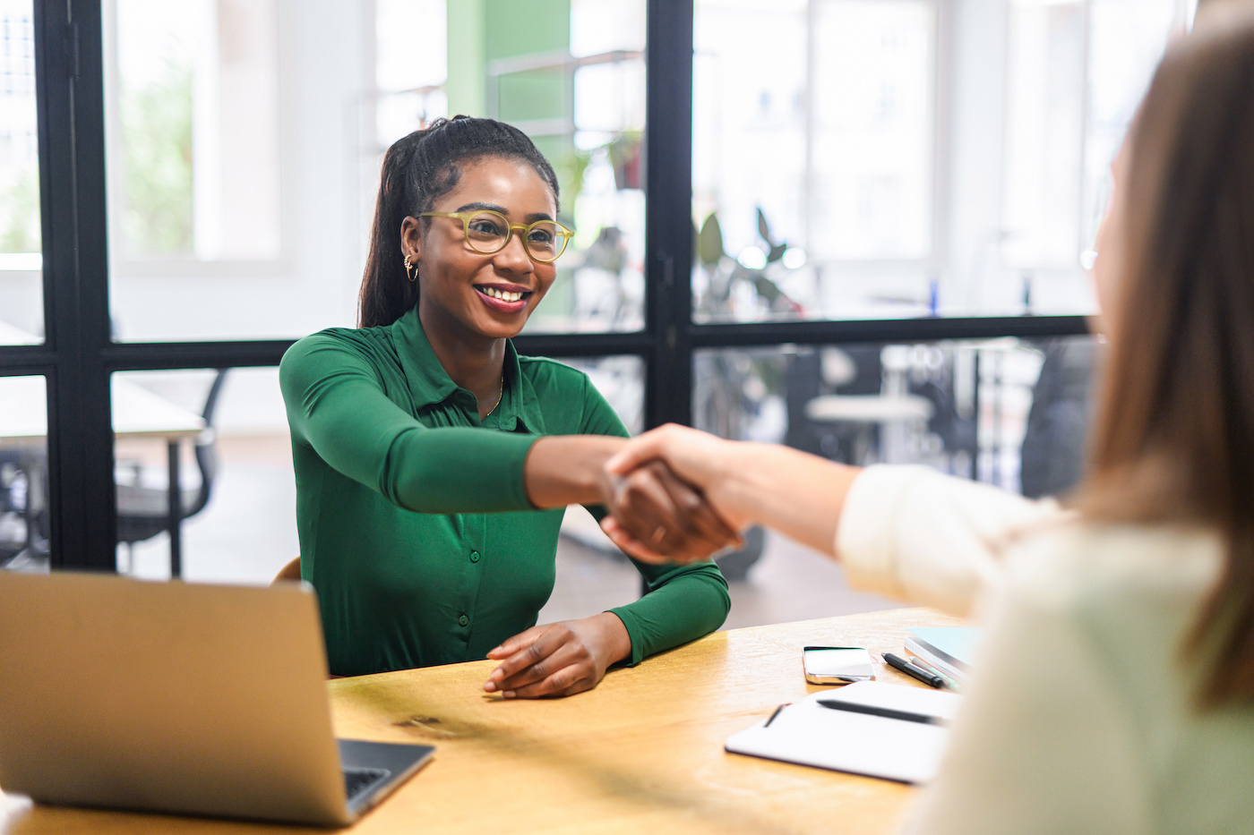 Two women shaking hands in a boardroom.