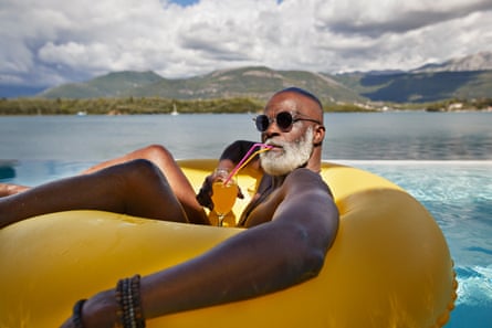 Man drinking juice in inflatable ringBald senior man wearing sunglasses while drinking juice in inflatable ring during vacation