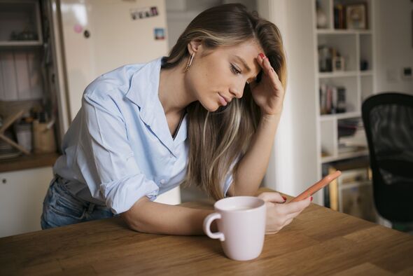 Young woman using her cellphone while drinking coffee in kitchen