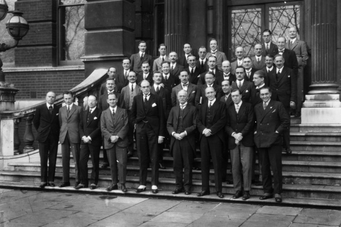 A group of men in suits stand on steps in front of a building