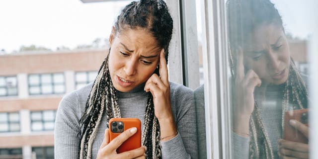 Stressed woman with hand on head, looking down at iPhone