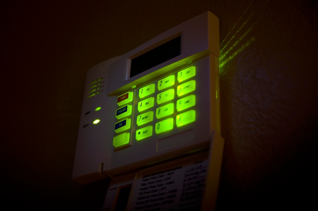 a security alarm keypad lit up with green buttons in a darkened room