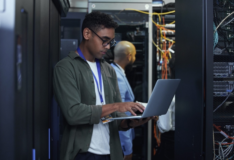 Ttwo male IT support agents working together in a dark network server room.