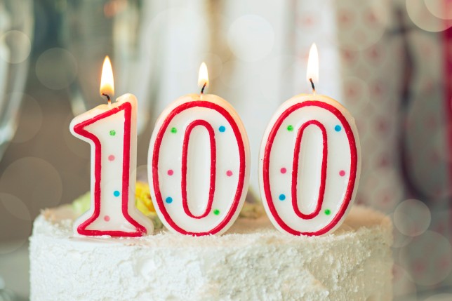 Birthday candle as number one hundred on top of sweet cake on the table, 100th birthday