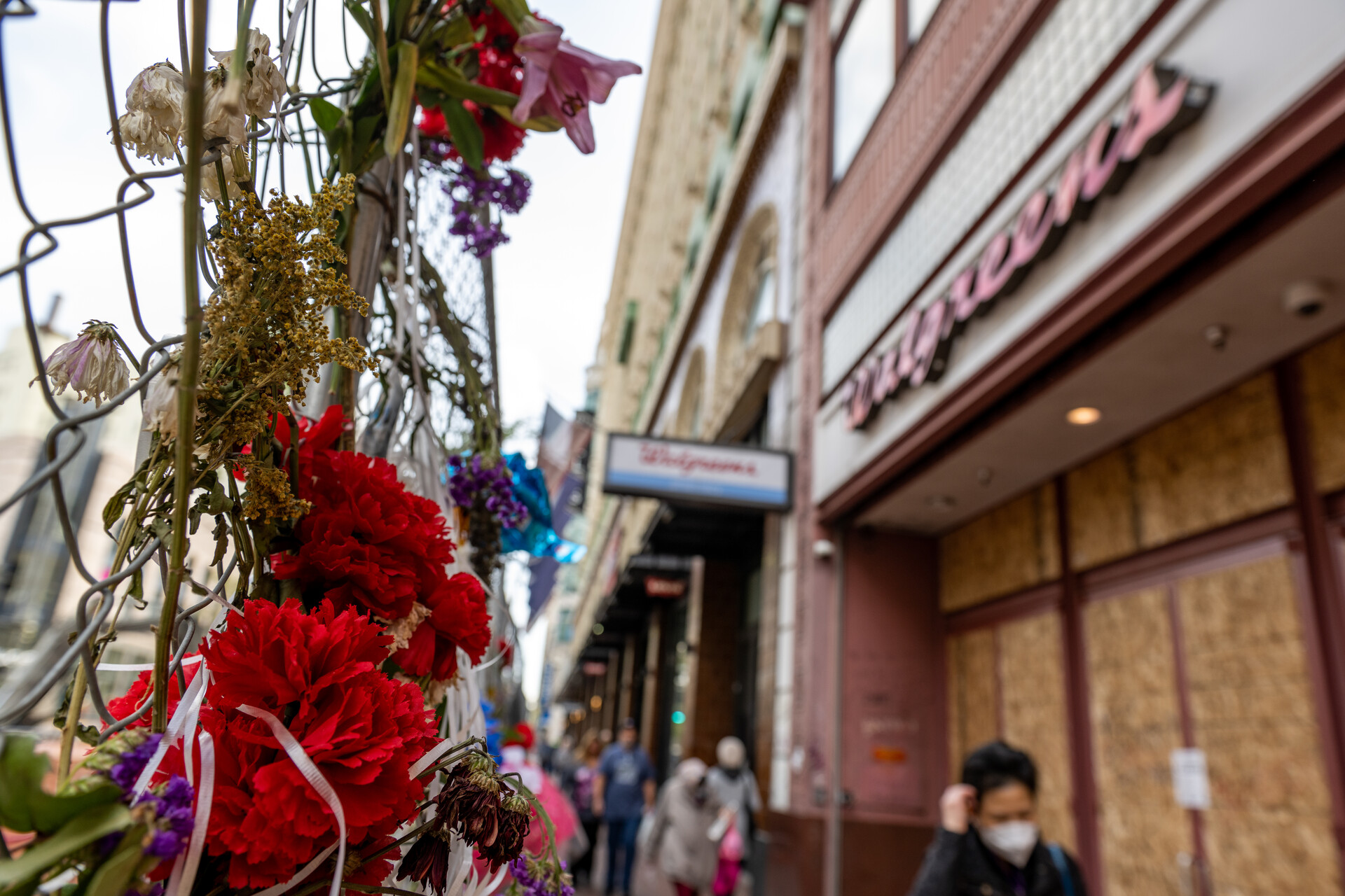 flowers and a memorial are tied to a fence with a Walgreens store in the background