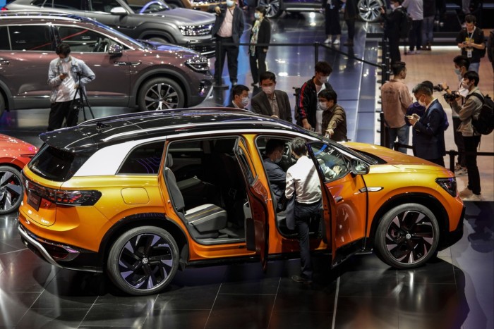 People inspect a new orange VW car at an auto fair