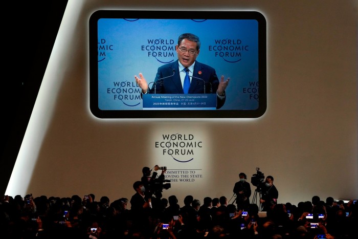 A middle-aged Asian man in a suit talks on a large screen at a conference hall 