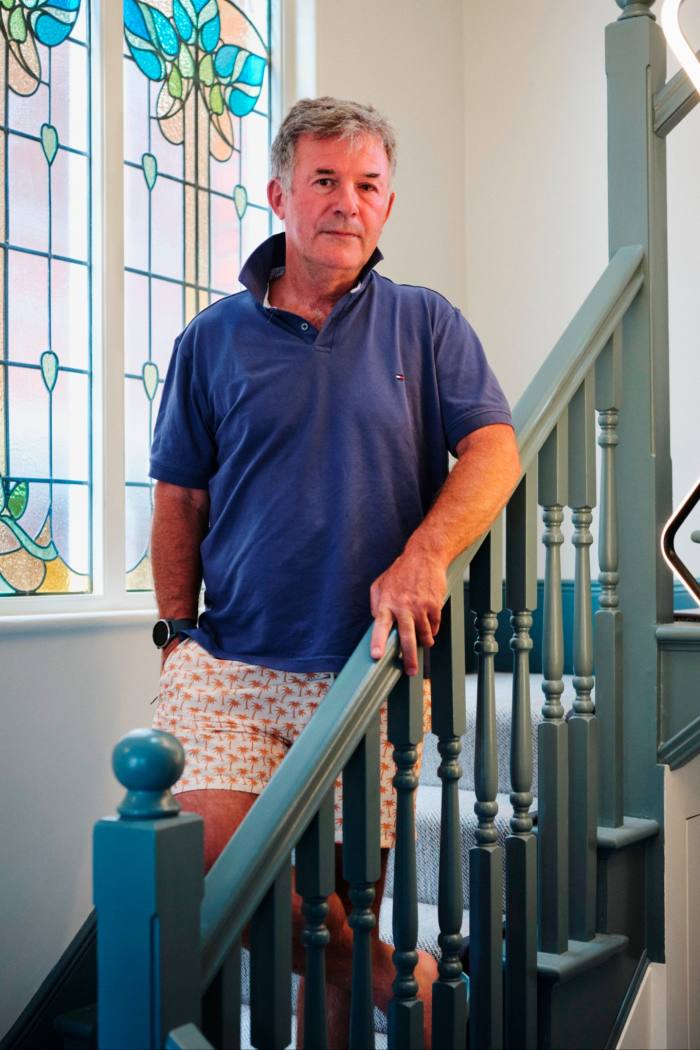 A man in polo shirt and shorts stands on a staircase by a stained-glass window
