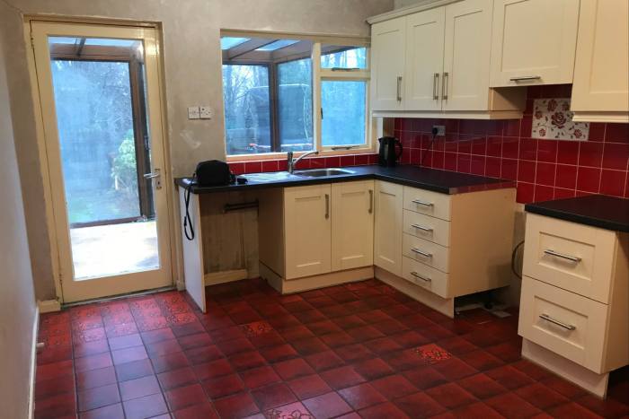 A dated kitchen with stained red tiles and door and wall separating the conservatory