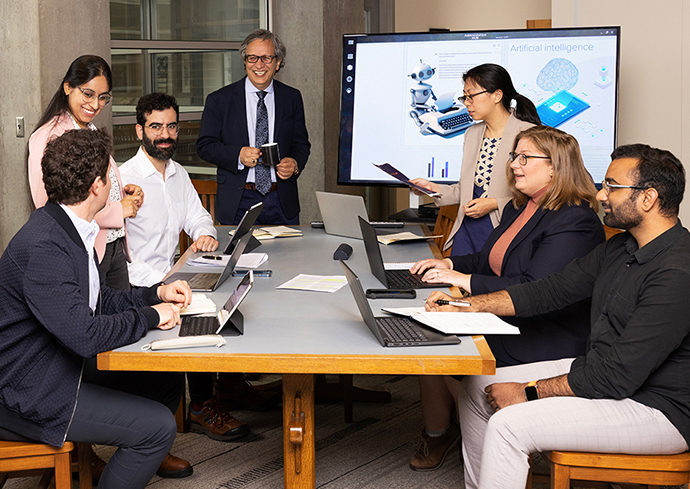 Group of individuals sitting around a table with several others standing talking.