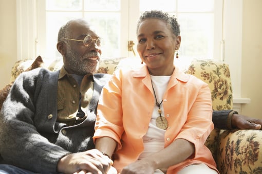 two older people sitting on a couch holding hands