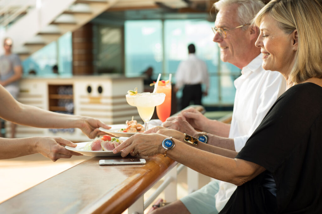 Two guests enjoy happy hour while sitting at a bar onboard a ship. 