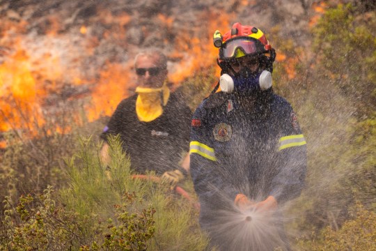 APOLLANA, GREECE - JULY 27: A firefighter is helped by a Czech emergency response team as they fight flames engulfing a hillside on July 27, 2023 in Apollana, Rhodes, Greece. Flames continue to spread on the island of Rhodes as Greece battles some 63 fires across the country during an intense heatwave. The fires on Rhodes prompted preventive evacuations of tens of thousands of tourists in the middle of the high summer season. (Photo by Dan Kitwood/Getty Images)