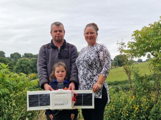 A family were stunned to find a UFO landed in their garden - and discovered it was a lost space balloon from Germany. Charlotte and Allen Buckley woke to see the 7ft long out-of-the-world object bouncing across their garden. And they carefully inspected to find it was a white box attached to a balloon with cameras fitted. The couple checked the marking to discover it was made by space company Solenix 560 miles away - and was lost in their garden in the countryside. It travelled from Darmstadt in Germany to Welsh countryside near the market town of Llanfair Caereinion in Powys. Pictured here Charlotte Buckley, husband Allen Buckley and daughter Lily Buckley holding the payload that landed in their field behinds them at Brook Valley Glamping WALES NEWS SERVICE