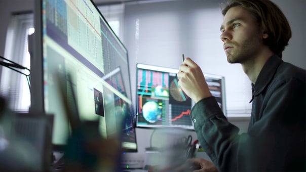 A person looking at charts and graph across multiple computer monitors