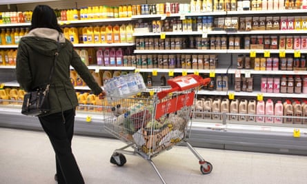 A person with shopping trolley in front of the dairy cabinet.