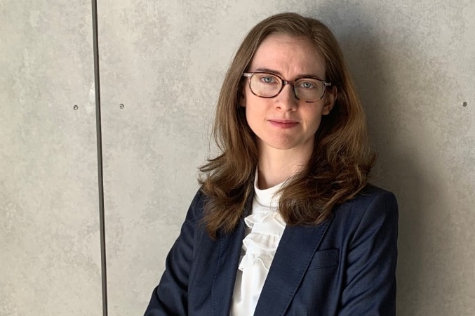 A woman stands against a concrete wall background.