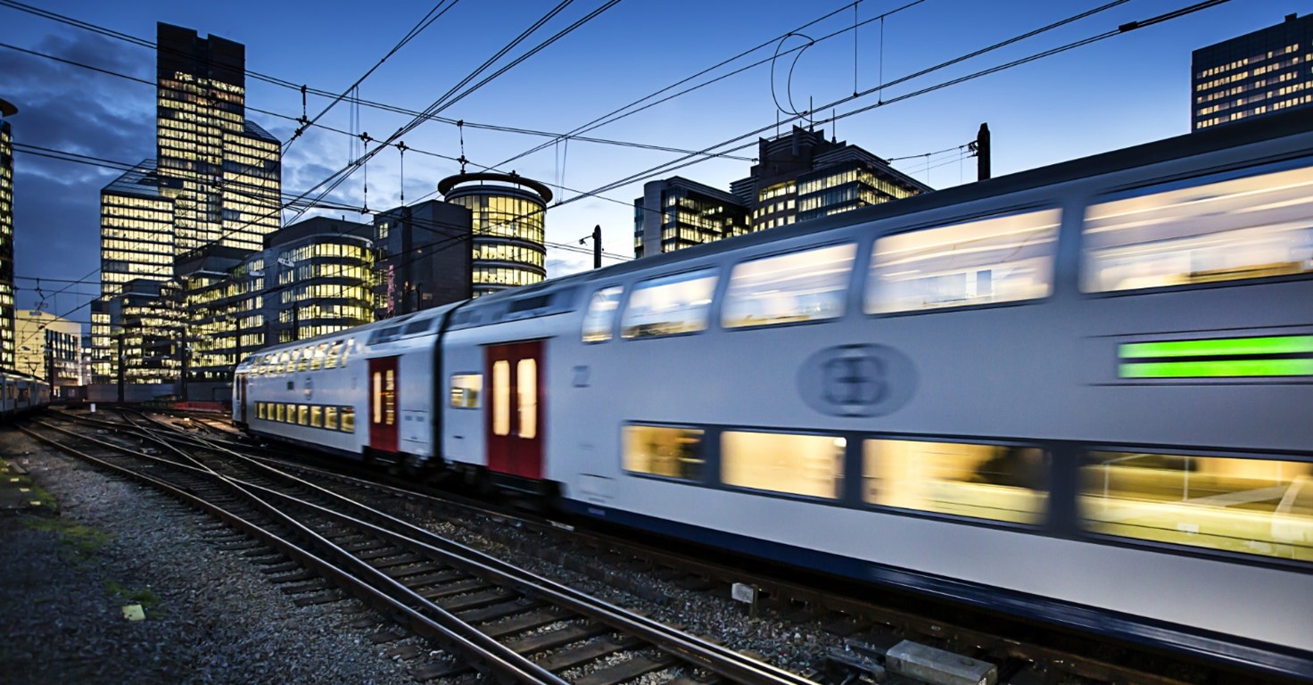 Railroad tracks with train rushing past in foreground with city skyline in the background. 