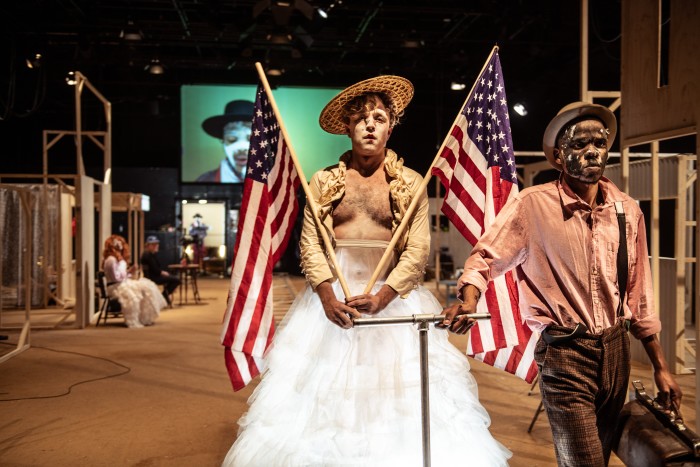 Two men stand dressed in strange attire holding Stars and Stripes flags