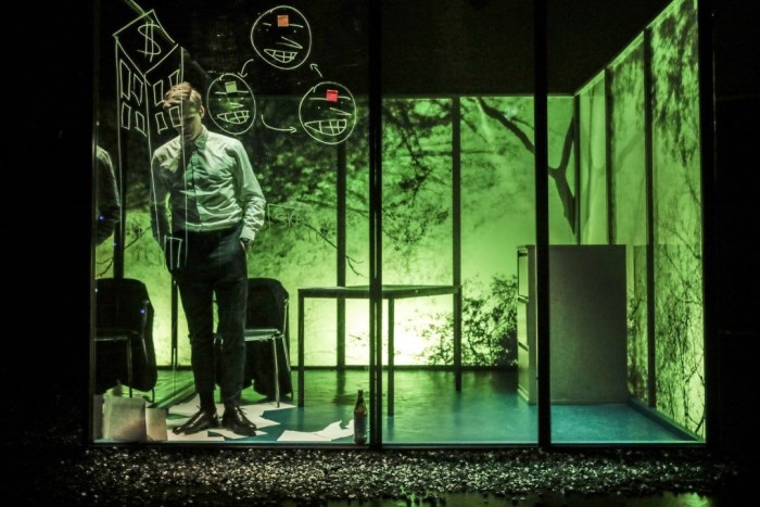 A man dressed in suit and tie stands inside an office that looks like a metal cage