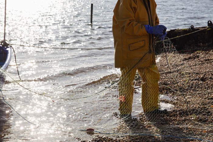 A fisherman, with only his torso, arms and lower body visible, on the shore holding a fishing net