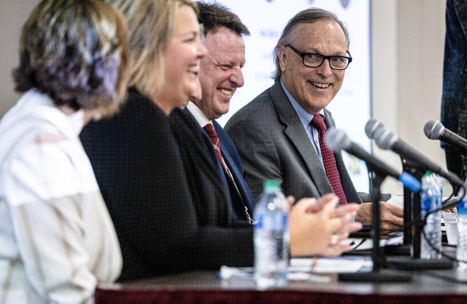 Group of four people sitting at long table talking and laughing during panel