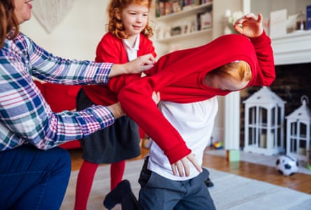 A mother helps her son put on his school uniform ready to start school that day with some help from his sister.