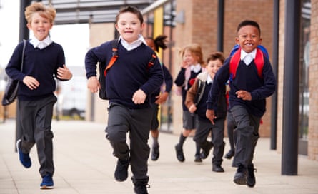 Excited primary school kids, wearing school uniforms and backpacks, run on a walkway outside their school building