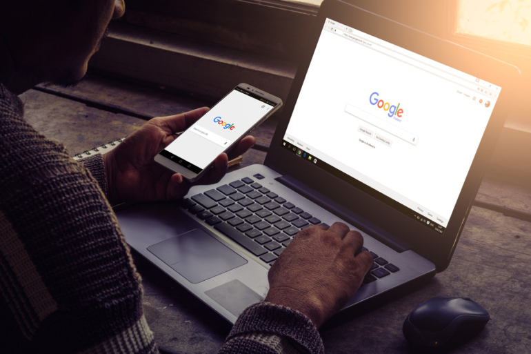 Man using both his laptop and mobile phone with Google on display.