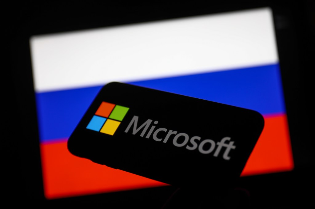 Microsoft logo displayed on a phone screen and Russian flag displayed on a screen in the background are seen in this illustration